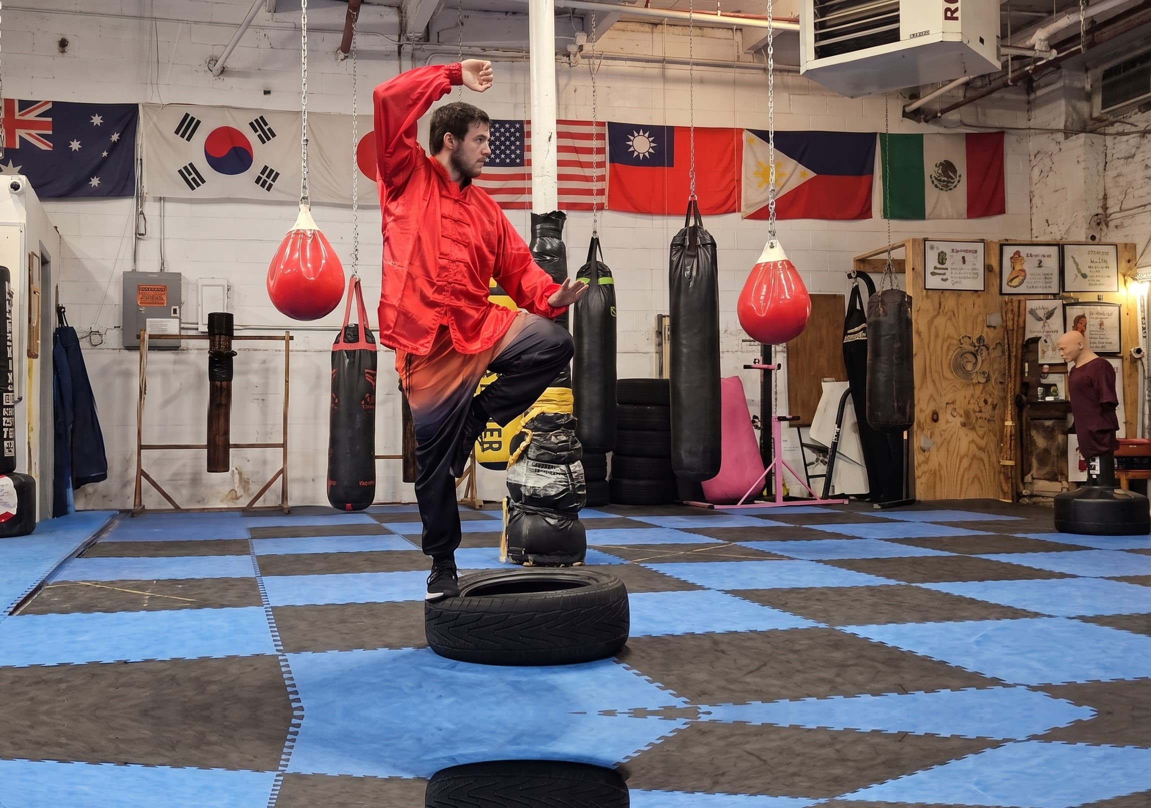 A Cloud Forest student in a red kung fu uniform balancing in crane stance on a tire in the training hall